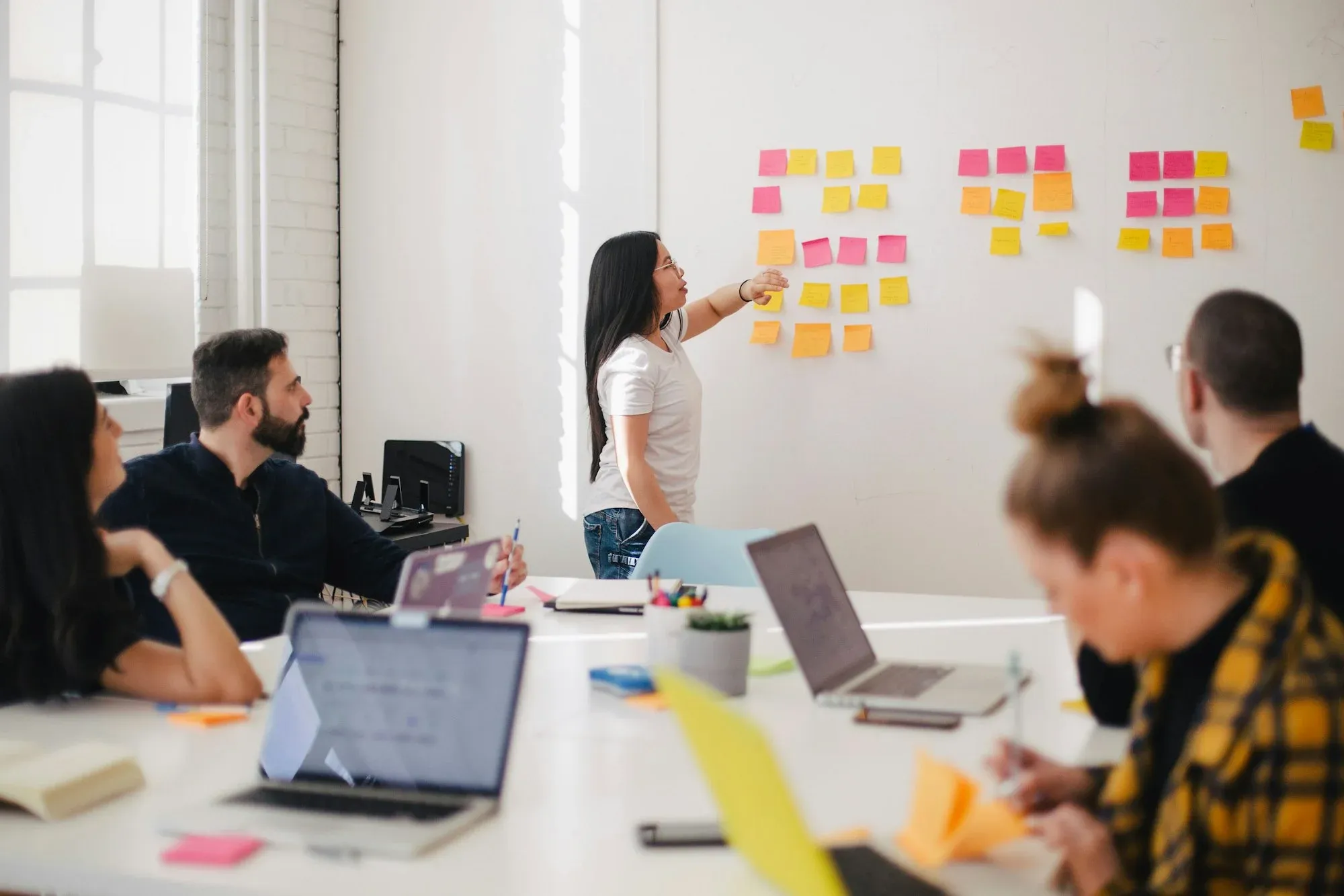 A team gathered around a table while a colleague maps out a plan on a wall of sticky notes